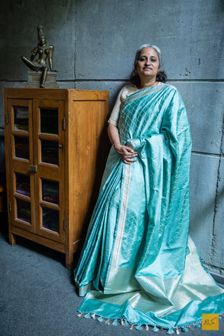 Elevate your wardrobe with this exquisite Sowbhagya saree. Crafted in a luxurious greenish blue hue from mashru silk, and adorned with intricate extra weft jaal design, as well as a riot of bright zari weave on the border and pallu, this banarasi handwoven saree is as luxurious as it is lightweight and easy to drape. An irresistible addition to your wardrobe.  Fabric- Mashru silk  Colour- Greenish Blue