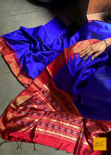Vagdevi is a handwoven dupion silk sari in dark blue and red. Adorned with a traditional temple border, this sari is perfect for special occasions and festivities. The combination of beautiful colors and intricate weaving make this sari a timeless piece of art.